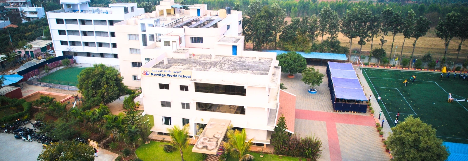 Aerial view of NewAge World School campus featuring modern buildings, lush greenery, and well-equipped sports facilities in Bangalore.
